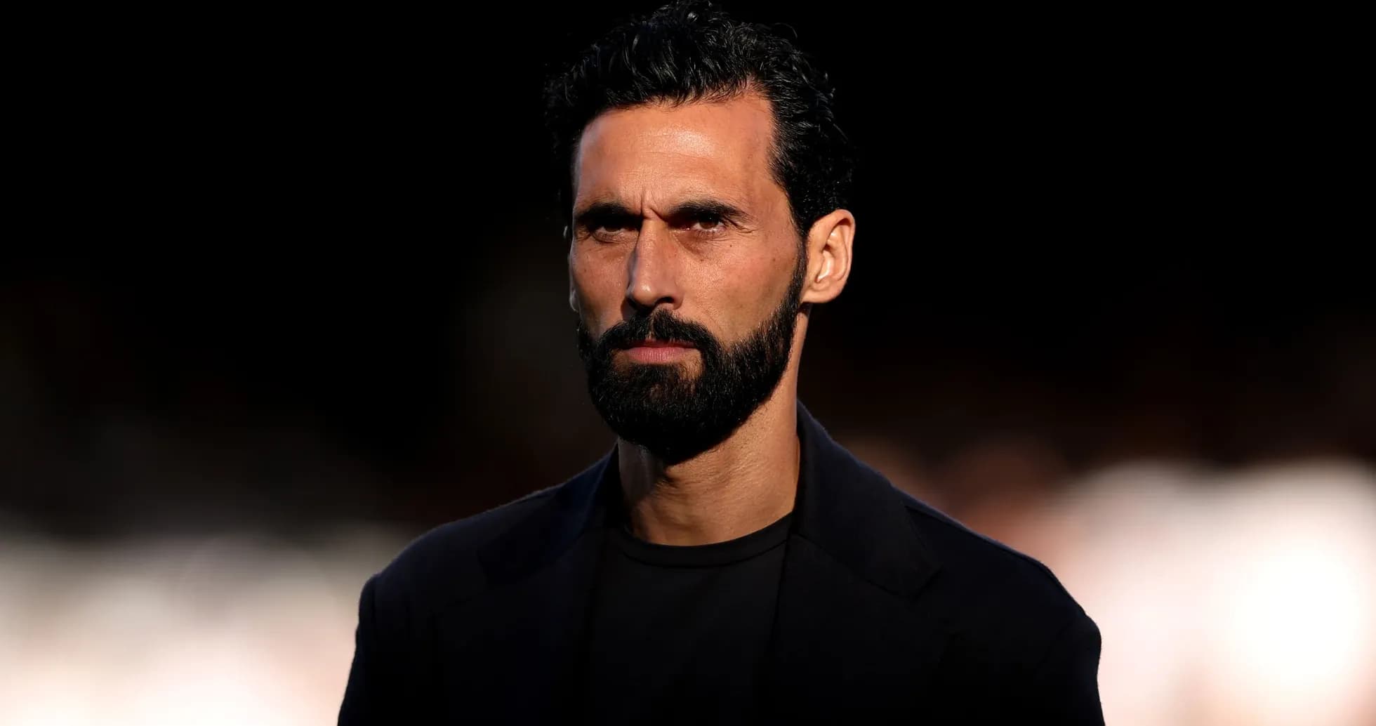 Man with beard and serious expression in dark attire