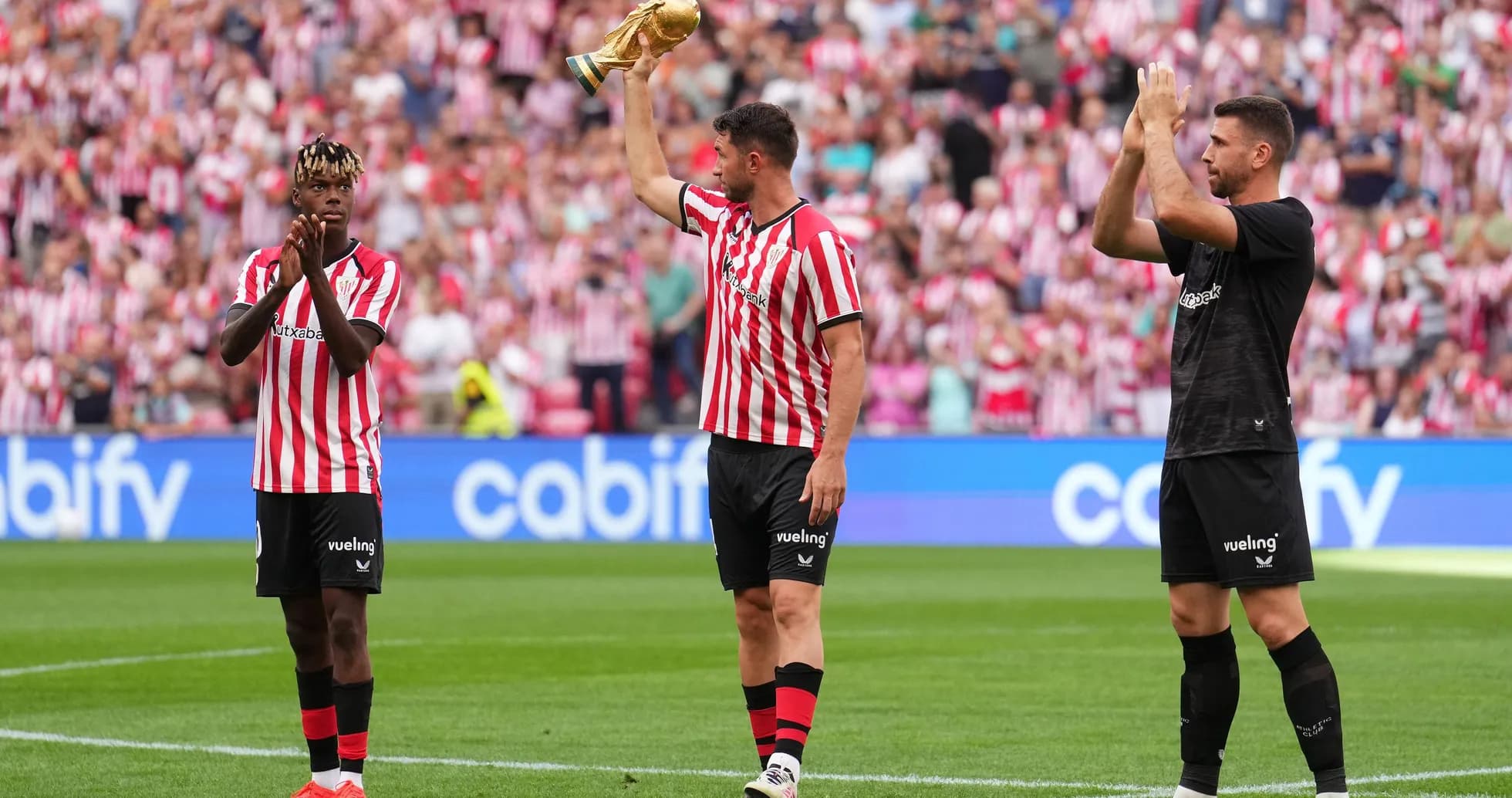 Player holding trophy while teammates applaud fans