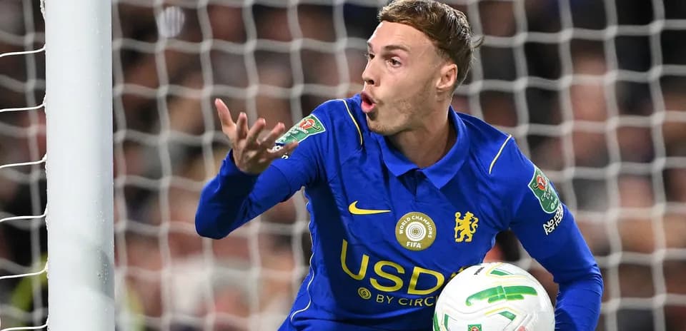 Futbolchi darvozaga to'pni ko'tarib gest qilmoqda