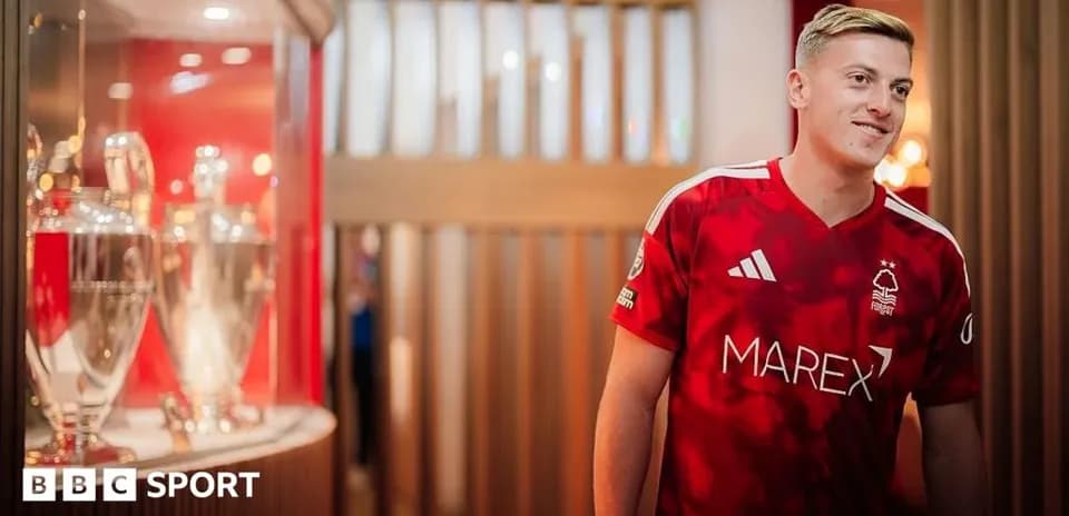 Futbolchi qizil formada kuboklar oldida turibdi