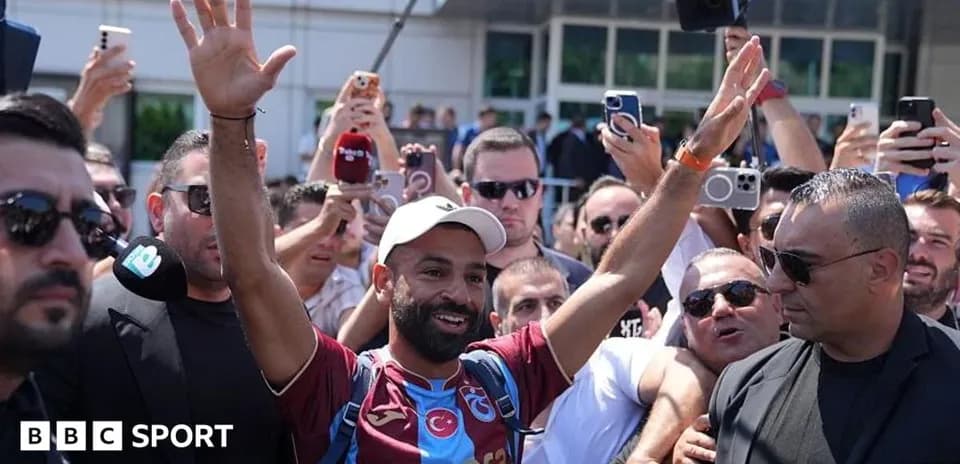Futbolchi muxlislar orasida qo'l ko'tarib turibdi