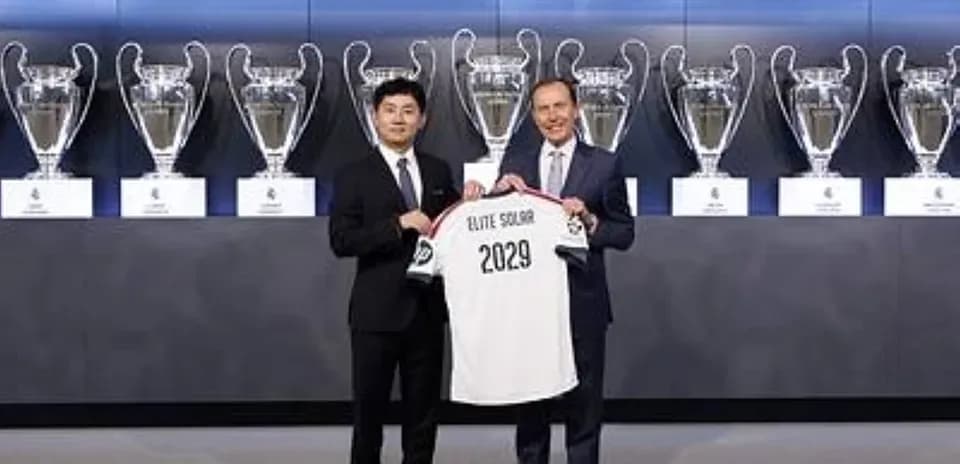 Two men holding a jersey in front of trophies