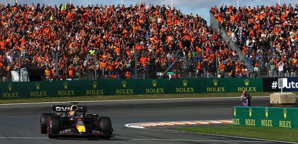 Formula 1 car racing past cheering orange-clad crowd