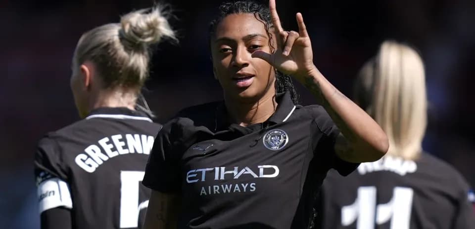 Futbolchi g'alaba belgisini ko'rsatmoqda, orqa fonda jamoa a'zolari