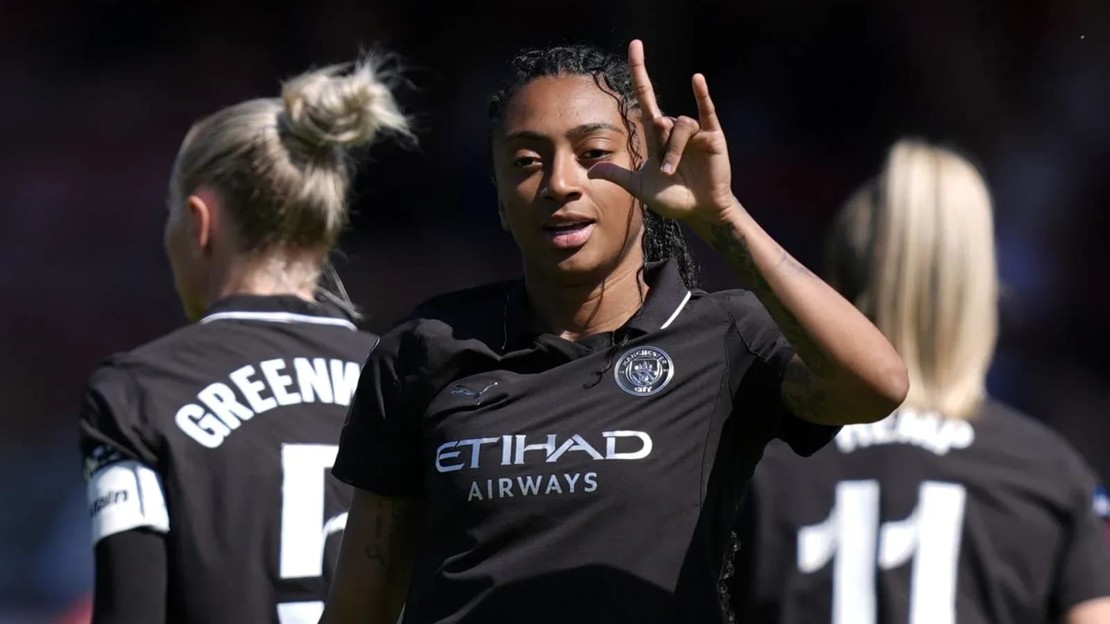 Futbolchi g'alaba belgisini ko'rsatmoqda, orqa fonda jamoa a'zolari