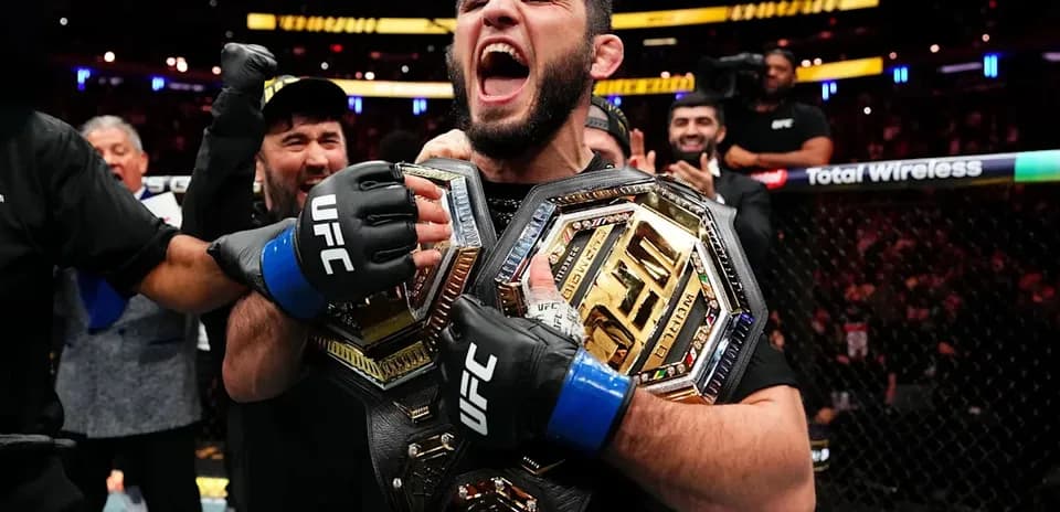 Fighter celebrating with two championship belts in octagon