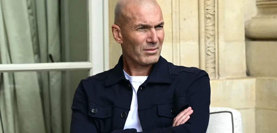 Bald man in navy jacket seated outdoors