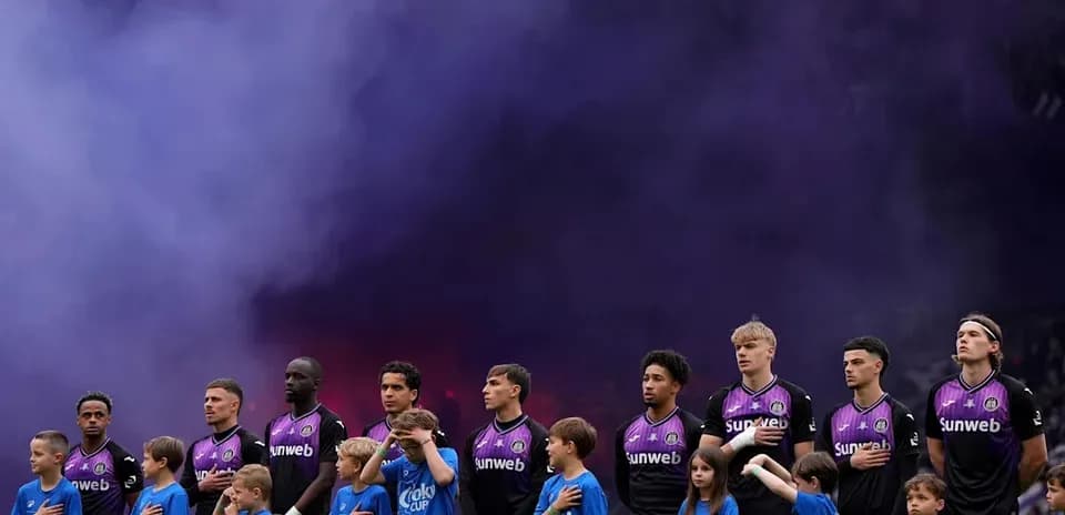 Futbolchilar va bolalar bayroq oldida turishmoqda