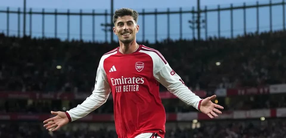 Futbolchi Arsenal formasida maydonda g'alaba nishoni ko'rsatmoqda