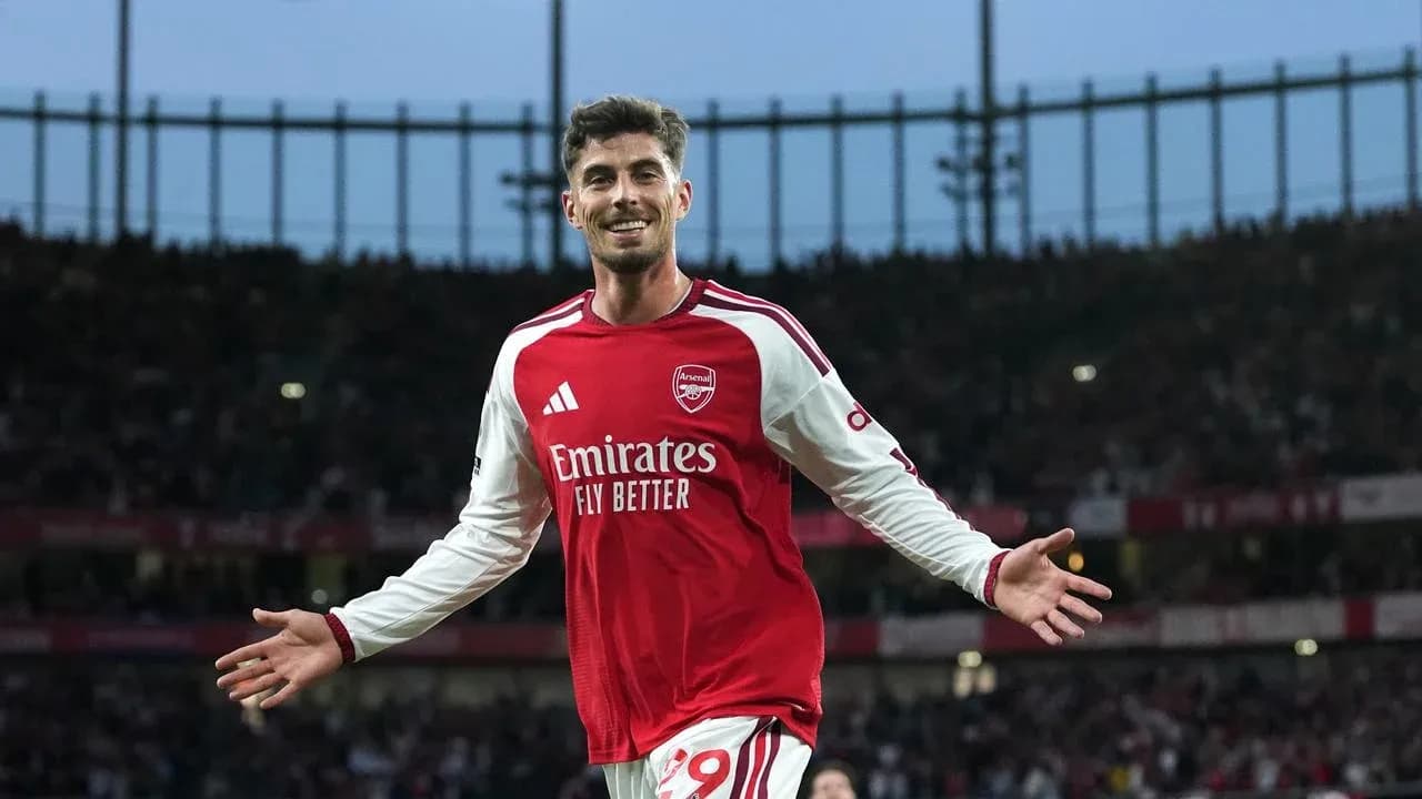 Futbolchi Arsenal formasida maydonda g'alaba nishoni ko'rsatmoqda