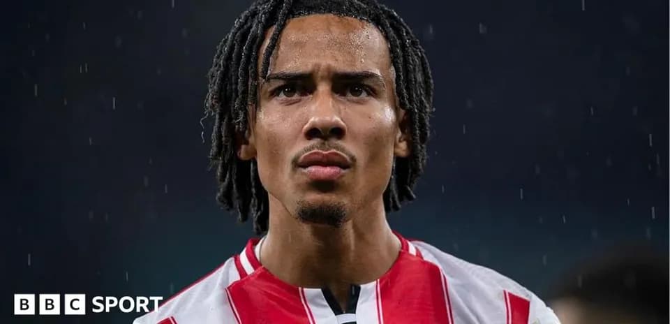 Futbolchi Brentford formasida, yomg'ir ostida turibdi