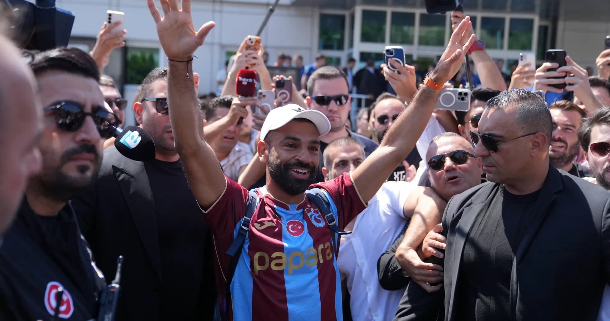 Futbolchi muxlislar orasida qo'l ko'tarib turgan