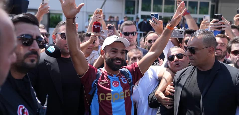 Futbolchi muxlislar orasida qo'l ko'tarib turgan