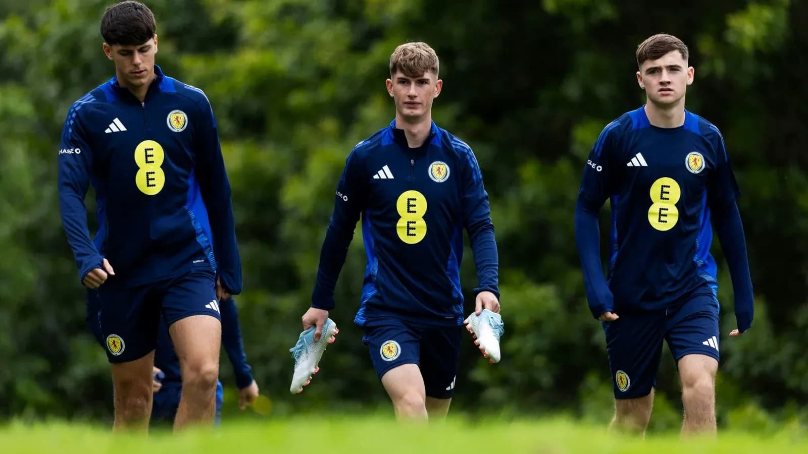 Three players walking in training kits with boots Three players walking in training kits with boots