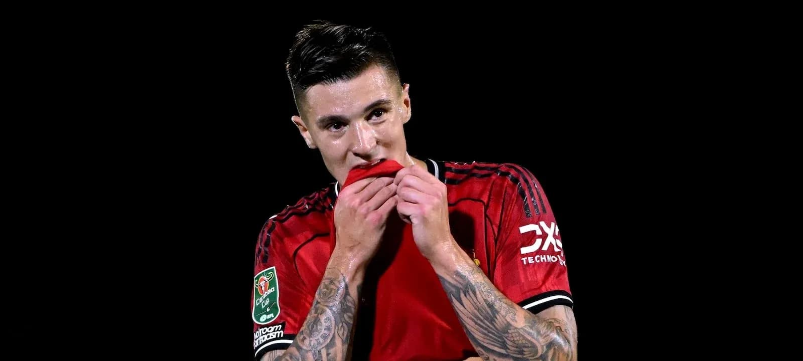 Futbolchi qizil forma kiyib, ko'ylagini tishlayapti Futbolchi qizil forma kiyib, ko'ylagini tishlayapti
